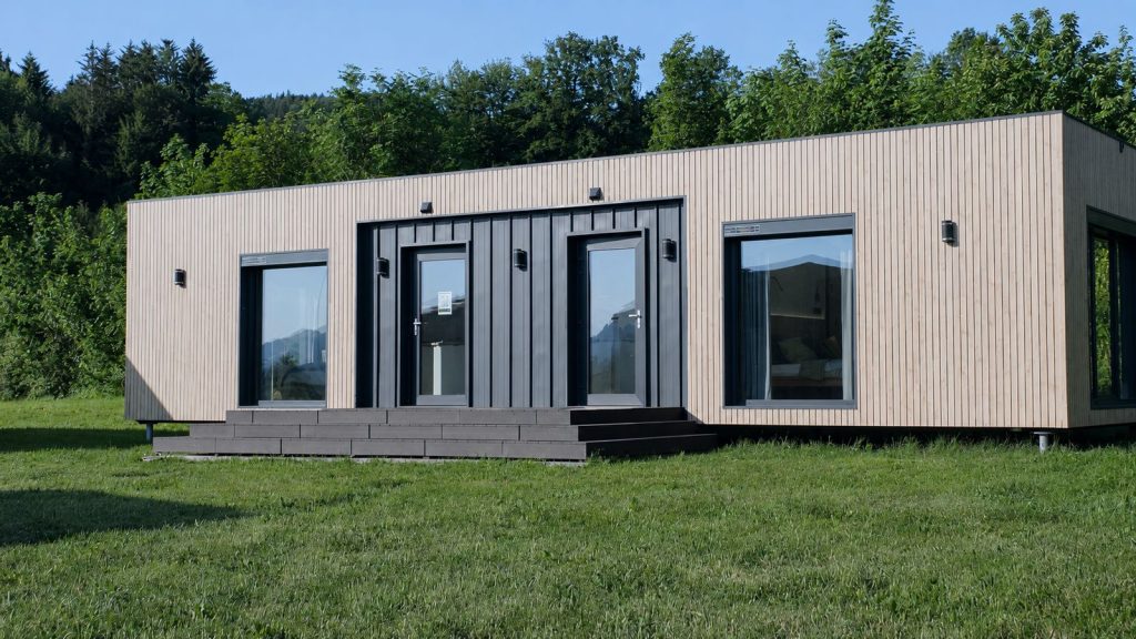 Alpenchalet mit heller Holzfassade und anthrazitfarbenem Eingang auf gepflegtem Rasen - Premium-Modulhaus, Lieferung in die Steiermark.
