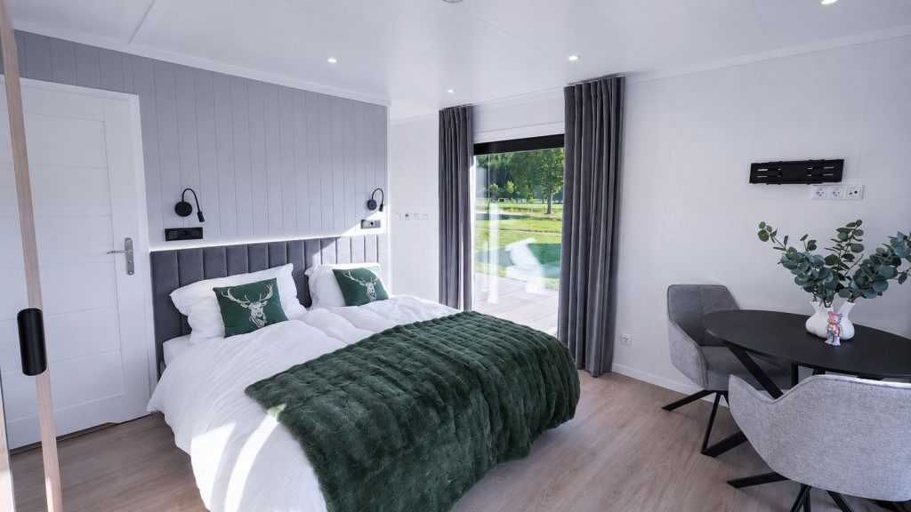 Vollmoebliertes Schlafzimmer mit Doppelbett, grauem Kopfteil und smaragdgruener Tagesdecke am Terrassenfenster.