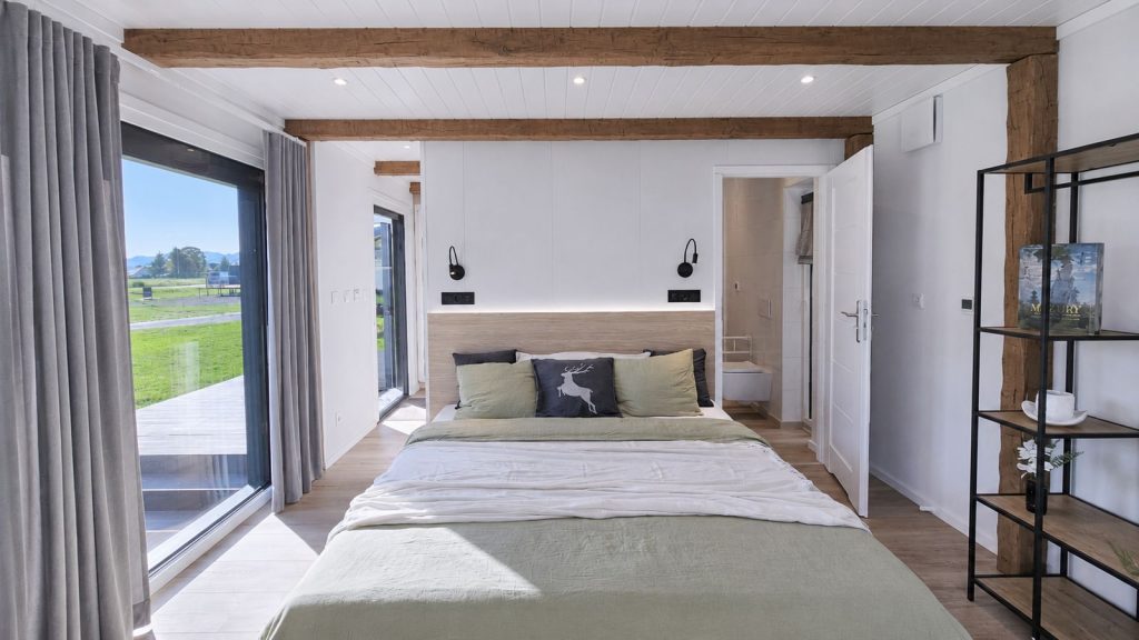 Schlafzimmer mit rustikalen Holzbalken, bodentiefer Terrassentuer und Ensuite - Ganzjahreshaus zur Lieferung nach Tirol.
