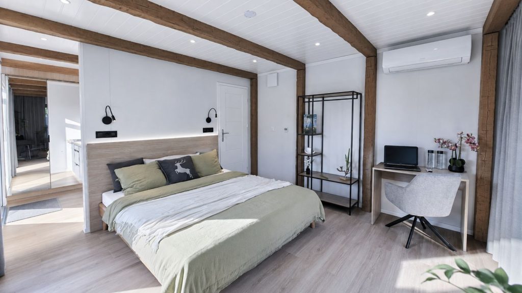 Gemuetliches Schlafzimmer mit rustikalen Holzbalken, Doppelbett und Arbeitsecke in einem BOND Fertighaus.