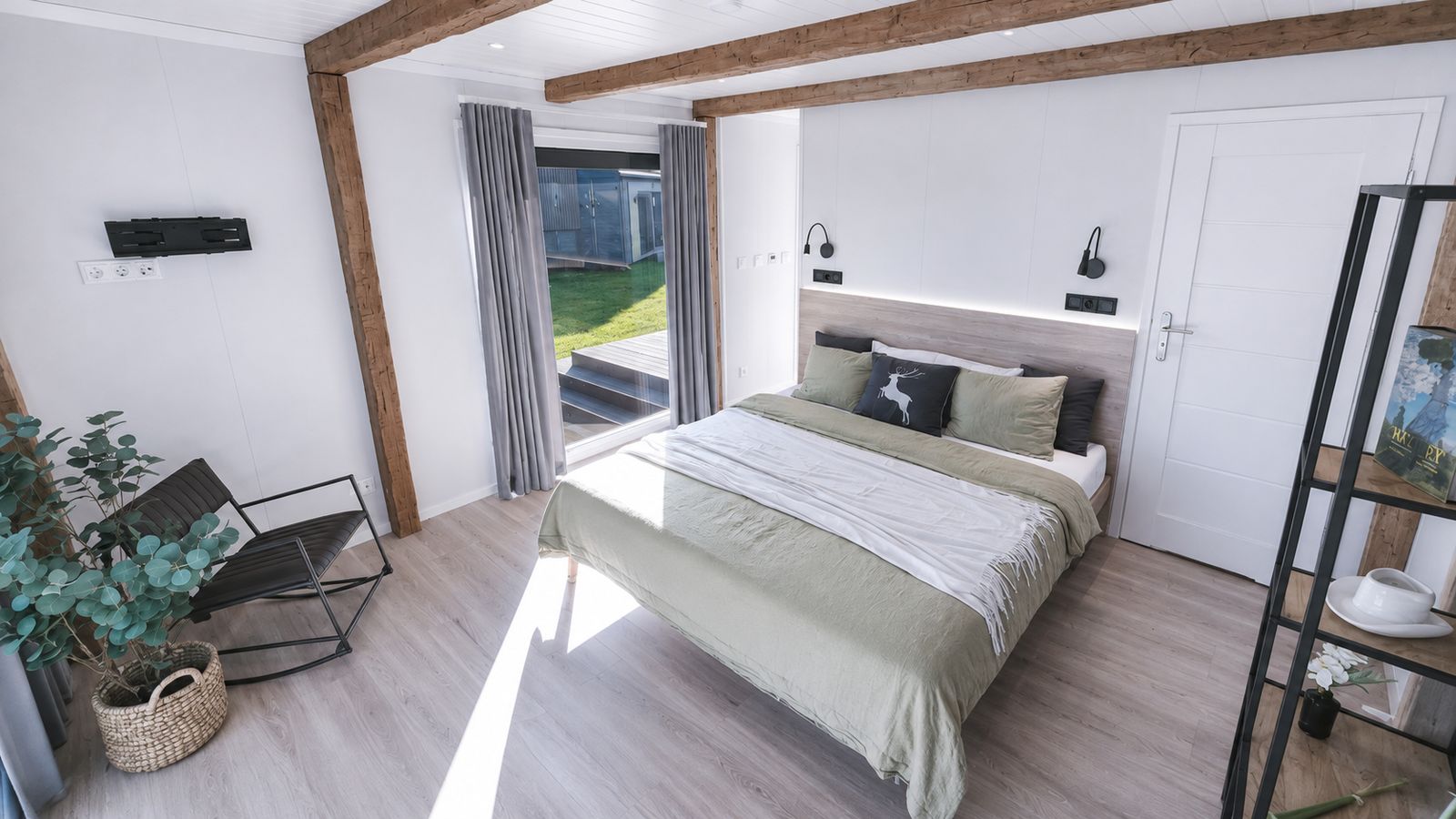 Gemuetliches Schlafzimmer mit Holzdeckenbalken, salbeigruener Tagesdecke und Terrassenzugang - Ganzjahreshaus, Lieferung nach Innsbruck.