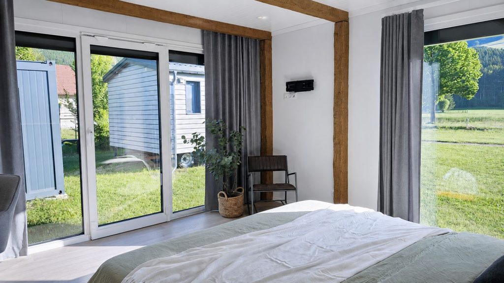 Schlafzimmer des Alpenchalet mit bodentiefer Schiebetuer, Holzbalken und Blick ins Gruene - wohnlich als Ganzjahreshaus.