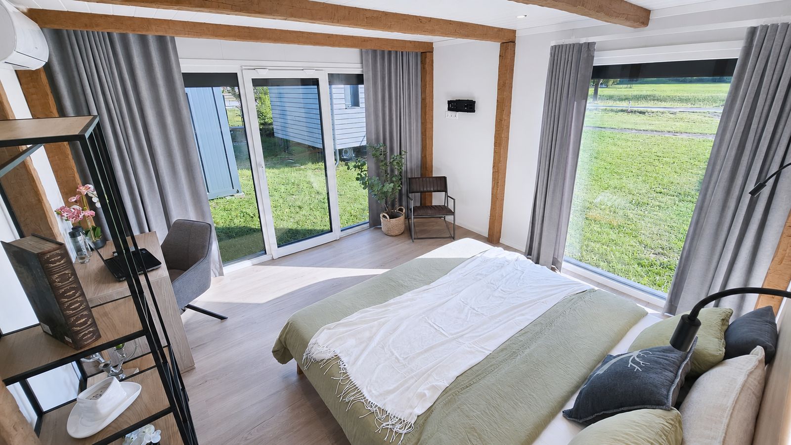 Schlafzimmer im Alpenchalet mit Holzbalken, gruenem Bett und Blick auf die Wiese - Modulhaus, Lieferung nach Tirol.
