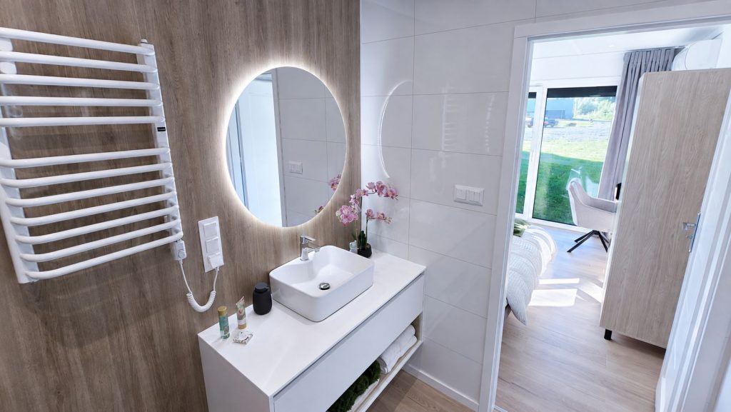 Badezimmer im Alpenchalet mit rundem LED-Spiegel, Aufsatzwaschbecken und Holzoptik-Wand - vollmoebliert, verfuegbar in Graz.