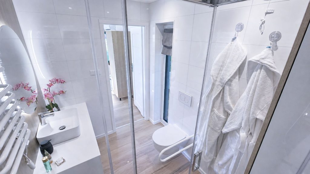 Weißes Bad im Alpenchalet mit Glasdusche, Waschtisch und Bademänteln - mobiles Eigenheim in Premiumqualität.