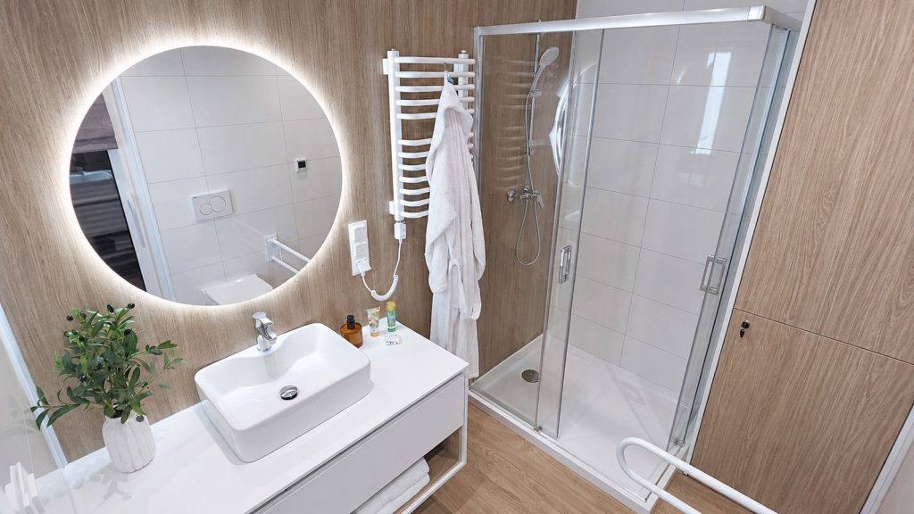 Badezimmer im Alpenchalet mit rundem LED-Spiegel, weissem Aufsatzwaschbecken und Glasdusche - schluesselfertig ausgestattet.