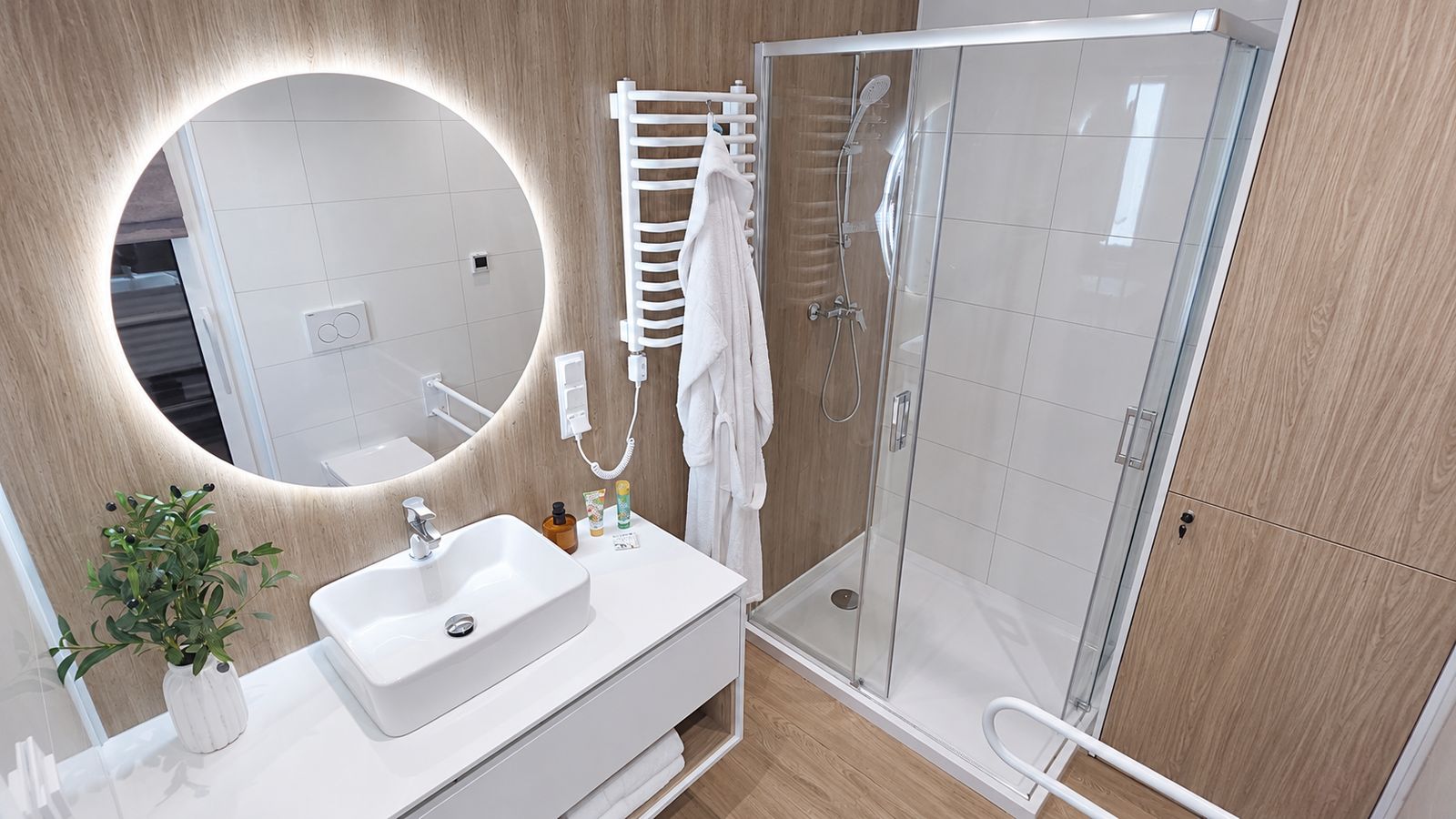 Badezimmer im Alpenchalet mit rundem LED-Spiegel, weissem Aufsatzwaschbecken und Glasdusche - schluesselfertig ausgestattet.