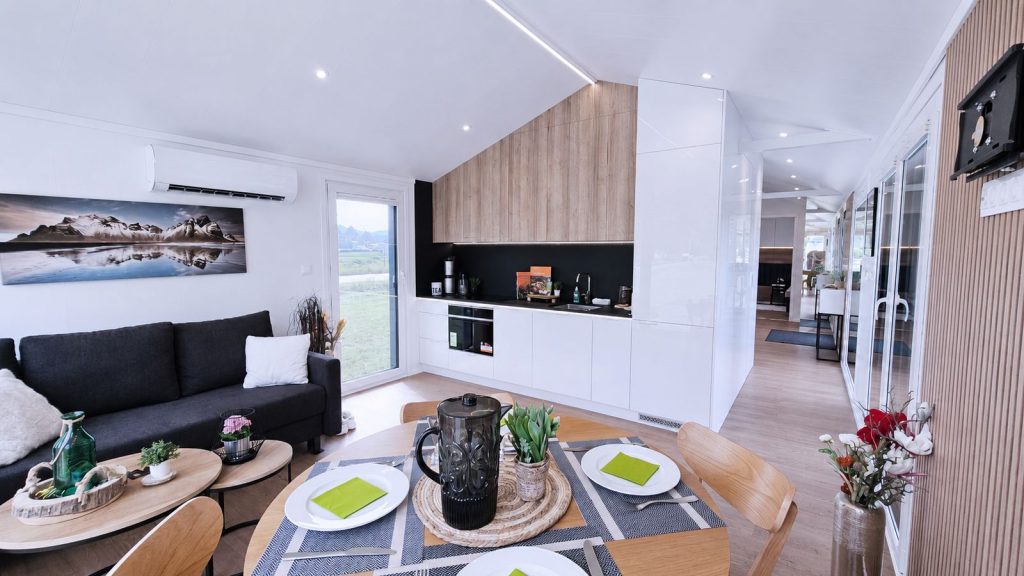 Offener Wohn-Ess-Bereich mit weisser Kueche, gedecktem Tisch und Bergfoto - Massivmodul-Architektur, verfuegbar in Linz.