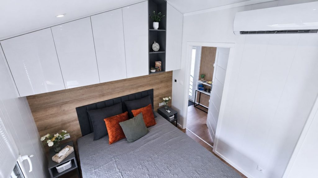 Schlafzimmer im Diamond Family Deluxe mit Holz-Akzentwand, Oberschränken und farbigen Kissen - Massivmodul-Architektur.