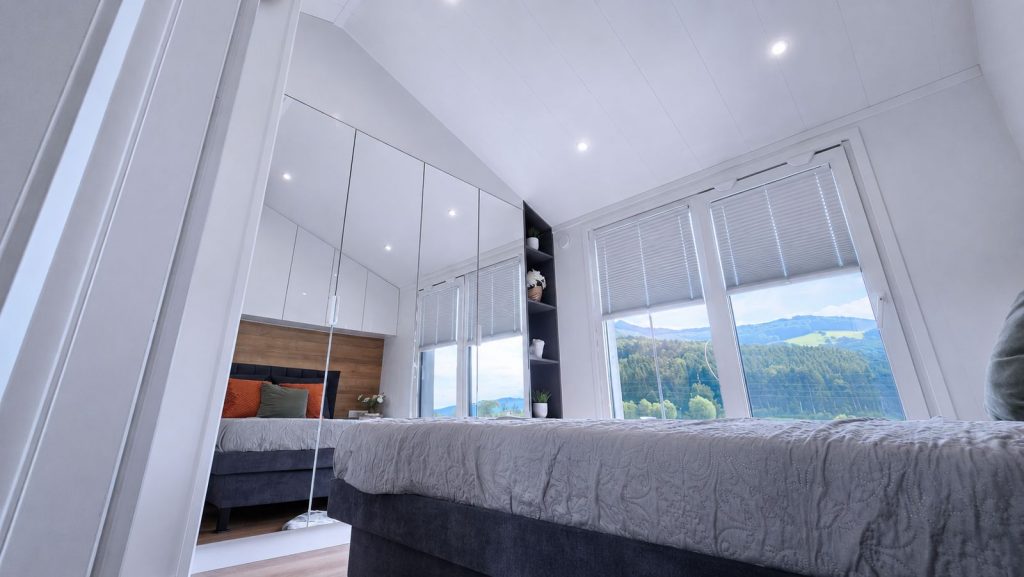Schlafzimmer mit dunkelblauem Bettsockel und Fenstern zur Huegellandschaft, in Massivmodul-Architektur, verfuegbar in Klagenfurt.