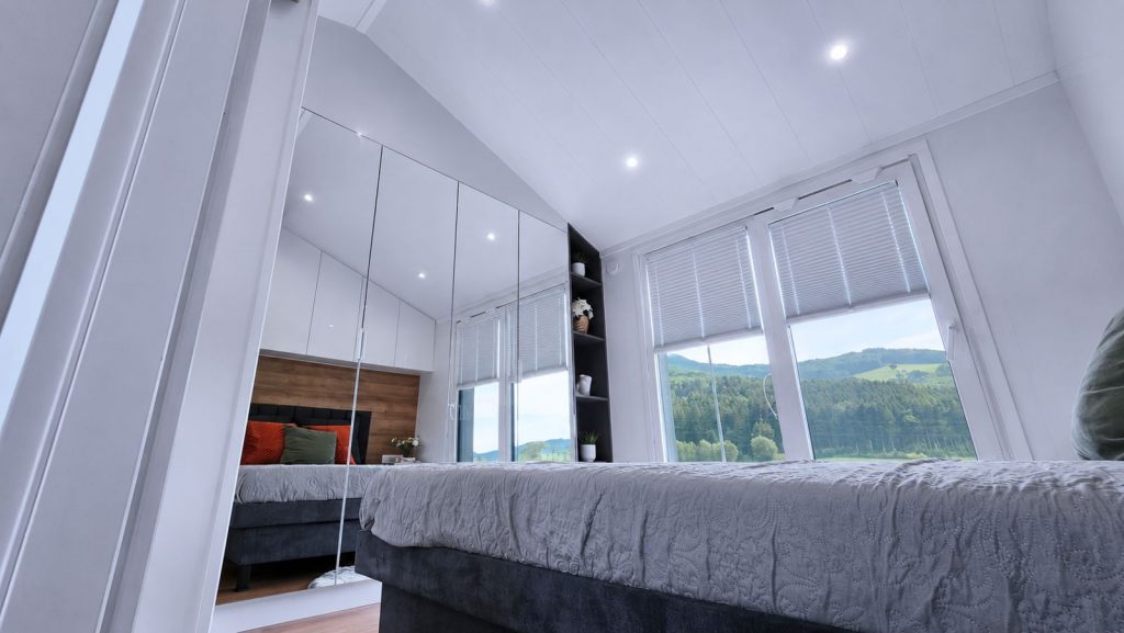 Schlafzimmer im Diamond Family Deluxe mit Spiegelschrank, Plissees und Blick auf gruene Huegel - wohnfertig ausgestattet.
