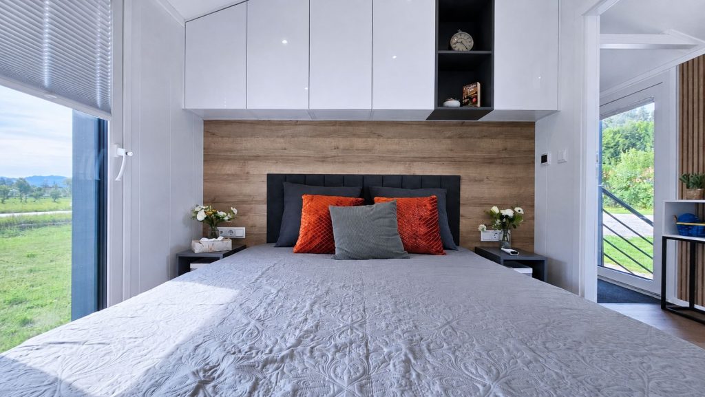 Schlafzimmer mit Doppelbett, Holzwand und orangefarbenen Kissen im Diamond Family Deluxe, modernes Eigenheim.