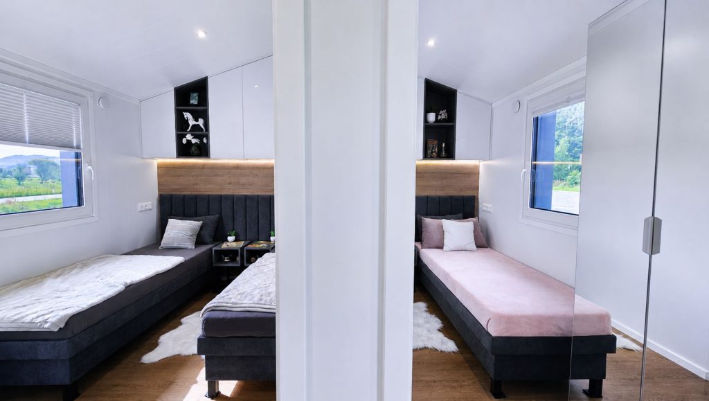 Kinderzimmer mit zwei Einzelbetten, rosa und weisser Tagesdecke sowie Regalnischen - Massivmodul-Architektur, verfuegbar in St. Poelten.