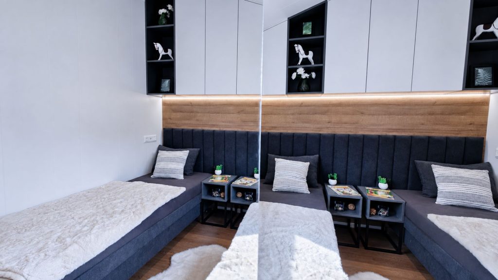 Kinderzimmer mit zwei Einzelbetten, dunklen Polsterlehnen und Schaukelpferd-Deko - Premium-Modulhaus, Lieferung nach Salzburg.