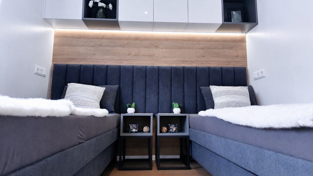Zweibettzimmer im Diamond Family Deluxe mit blauem Polsterkopfteil und LED-Oberschraenken - Modulhaus von BOND.