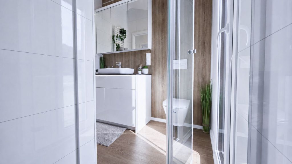 Badezimmer mit Glasdusche, Wand-WC und Holzoptik-Wand hinter Hochglanz-Waschtisch - komfortables Premium-Mobilheim.