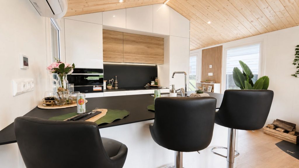 Kuechenzeile mit Bartheke, schwarzen Lederhockern und Holzdecke, wohnfertig eingerichtet mit Klimageraet und Naturholz.