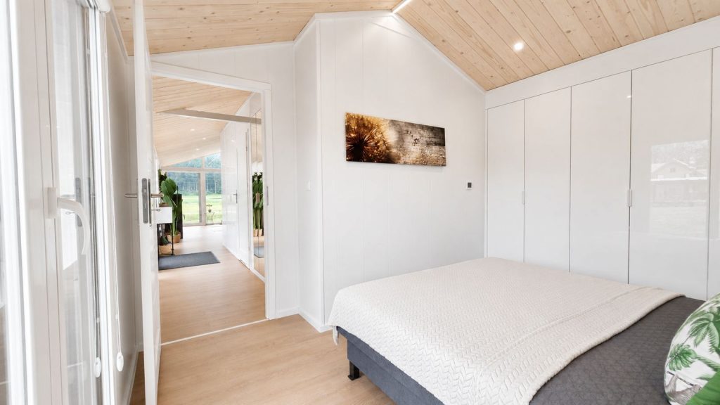 Modernes Eigenheim: Schlafzimmer mit Holzdecke, weissem Kleiderschrank und Ausblick in den Wohnraum.