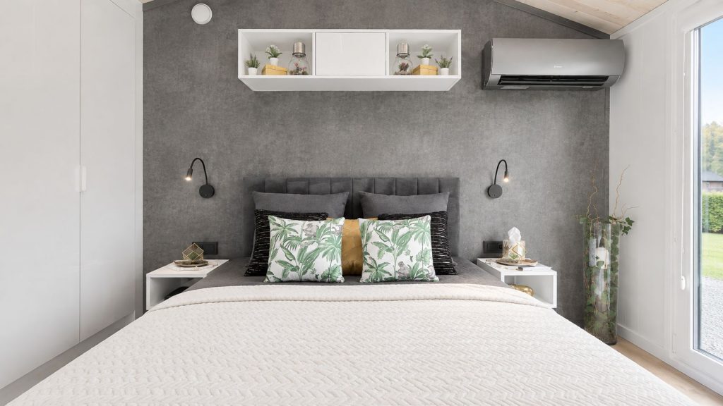 Schlafzimmer im Diamond +Plus mit Betonoptik-Wand, tropischen Akzentkissen und Klimageraet - Fertighaus in Premiumqualitaet.