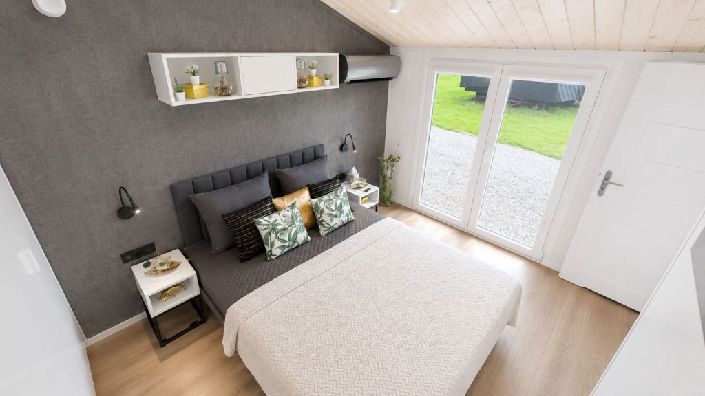 Schlafzimmer mit grauer Akustikwand, gepolstertem Bett und Terrassentür ins Grüne - wohnfertig eingerichtet.