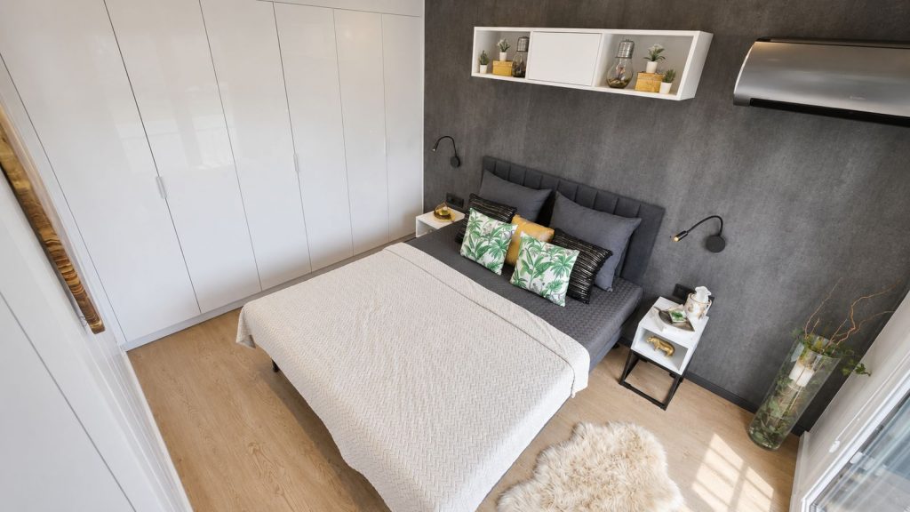 Schlafzimmer mit gepolstertem Kopfteil, dunkler Akzentwand und weissem Kleiderschrank - schluesselfertig ausgestattet.