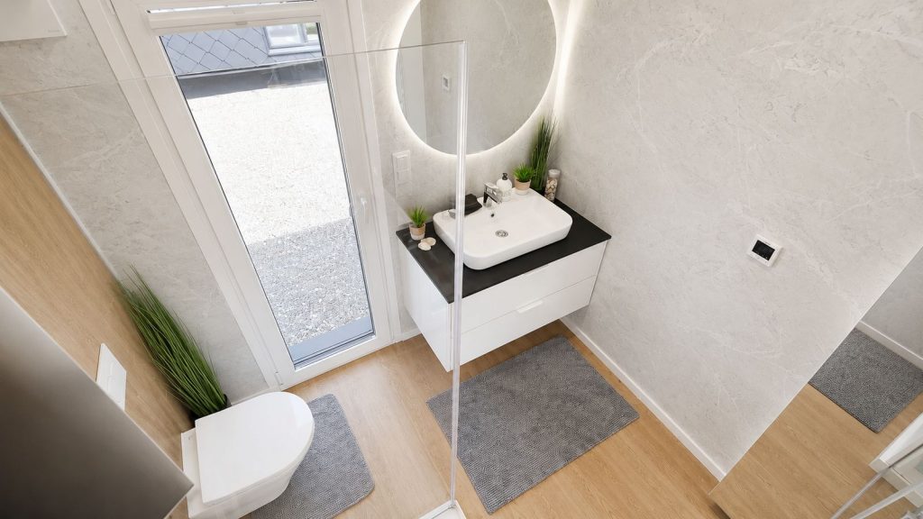 Wohnfertiges Bad in Marmoroptik mit rundem LED-Spiegel und Aufsatzwaschbecken, verfügbar in Salzburg.