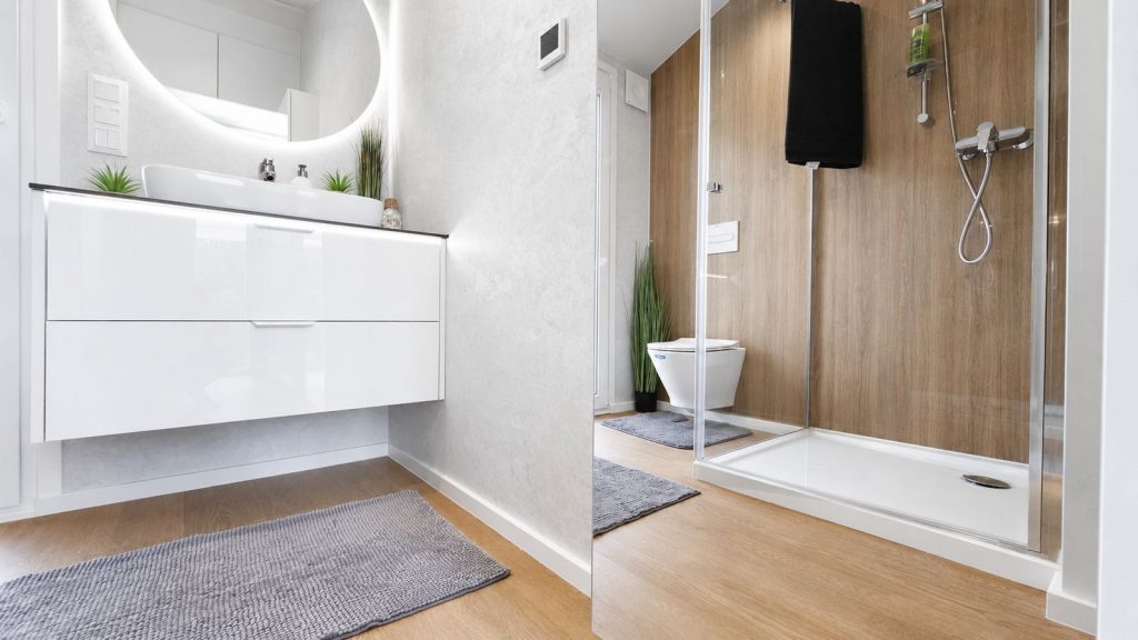 Badezimmer im Fertigteilhaus Diamond +Plus mit rundem LED-Spiegel, Hochglanzwaschtisch und begehbarer Dusche.