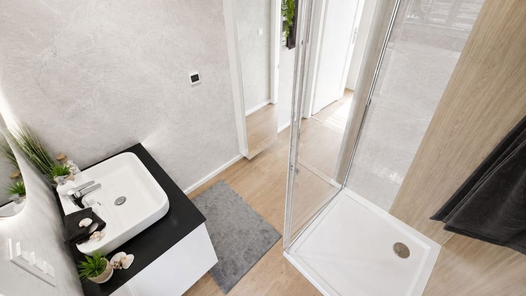 Badezimmer von oben mit Aufsatzwaschbecken, Marmoroptik-Wand und Duschkabine mit Glastuer - modernes Eigenheim vom Produzenten.