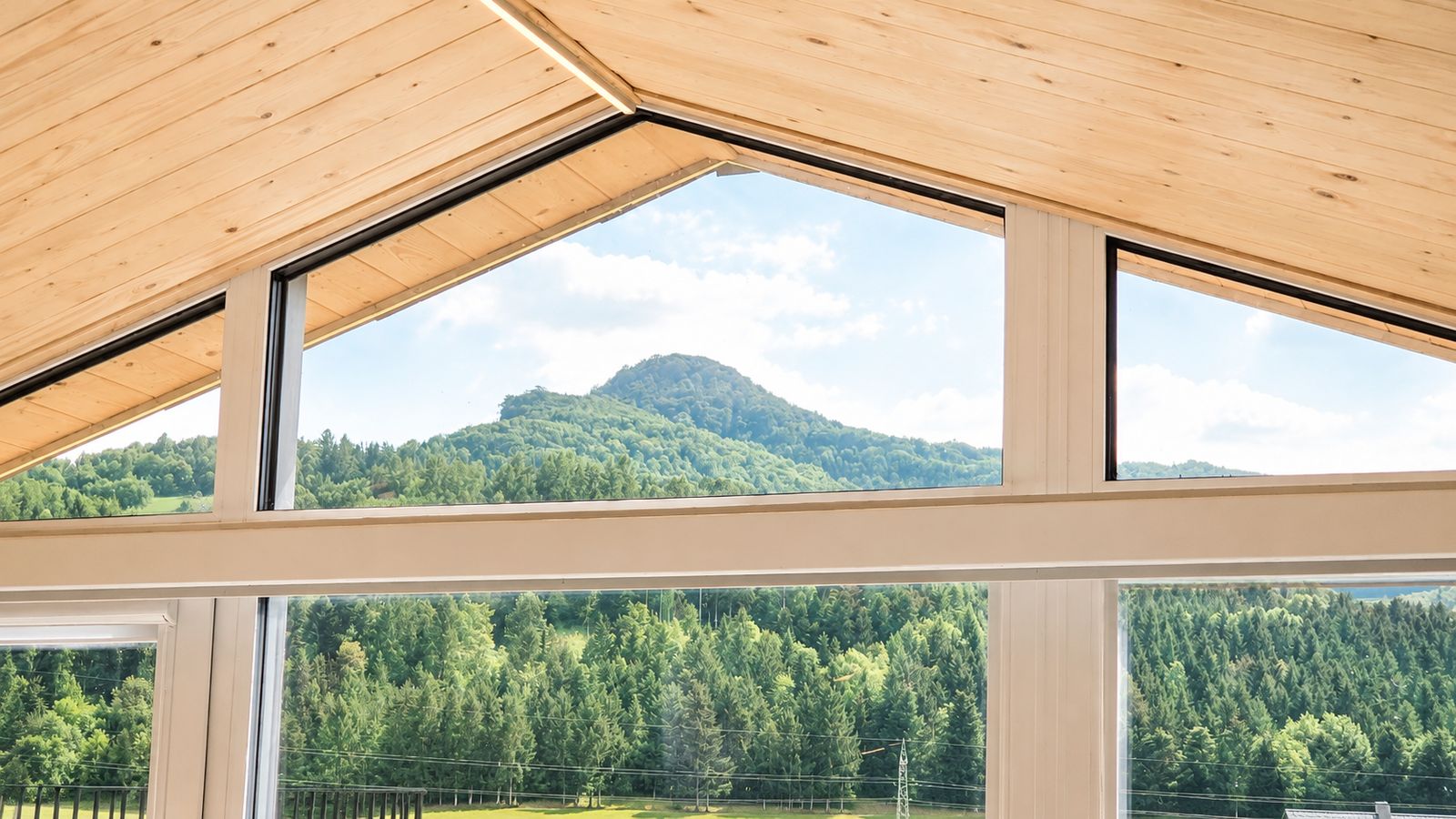 Giebelverglasung mit heller Holzdecke und Panoramablick auf bewaldete Berge - Premium-Modulhaus fuer Kaernten.