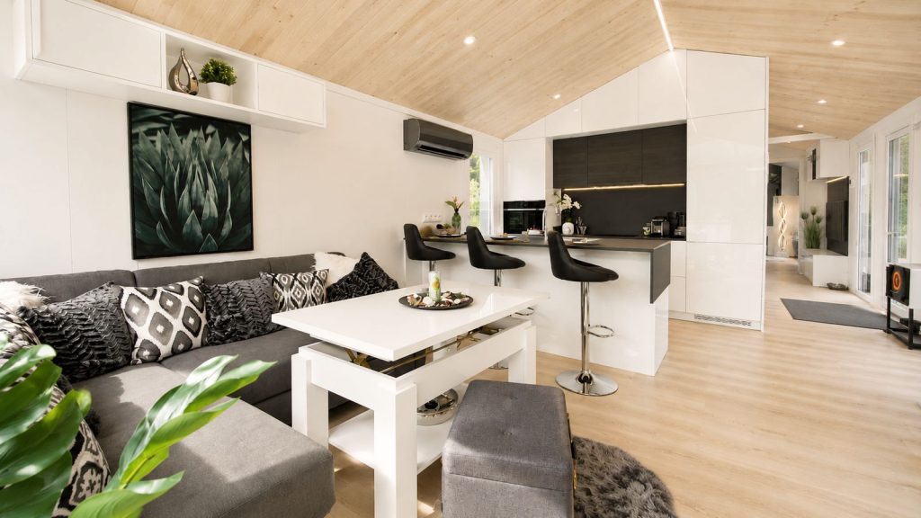 Offener Wohn-Koch-Bereich im Diamond +Plus Deluxe mit Holzdecke und L-Sofa - Fertighaus, verfuegbar in Wien.