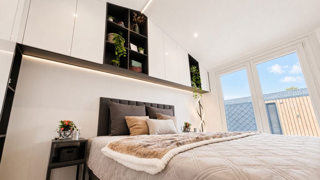 Wohnfertiges Schlafzimmer mit offenen Regalen, weichem Kopfteil und grosser Fensterfront, Lieferung nach Linz.