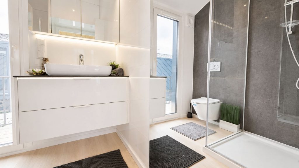 Helles Bad mit Aufsatzwaschbecken, Spiegelschrank und grau gefliester Dusche - Fertighaus in Premiumqualitaet.