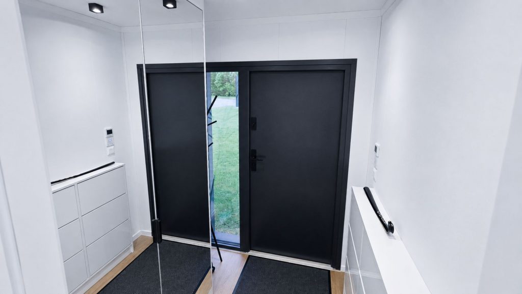 Eingangsbereich im Diamond Vario Deluxe mit schwarzer Haustür, Spiegelwand und Sideboard, modernes Eigenheim für Innsbruck.