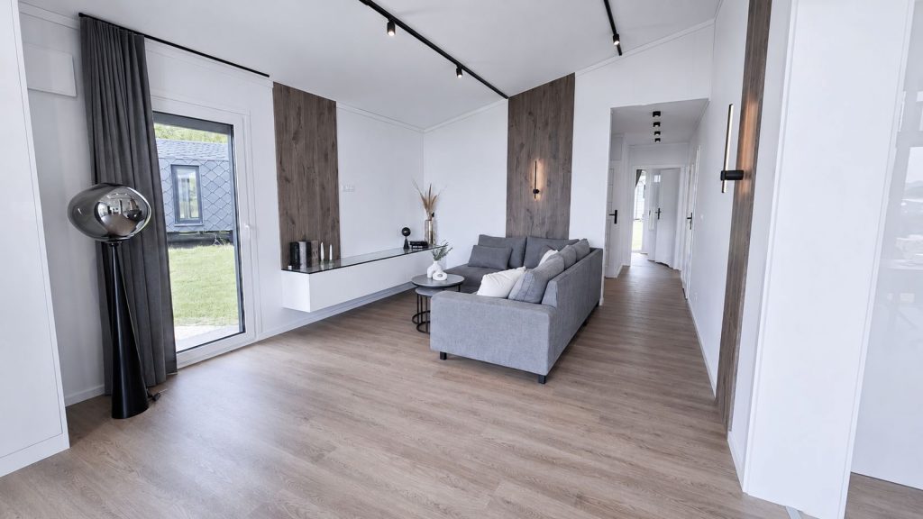 Wohnzimmer mit grauem Sofa, Holzpaneelen und Designer-Stehlampe - mobiles Eigenheim mit Lieferung nach Innsbruck.