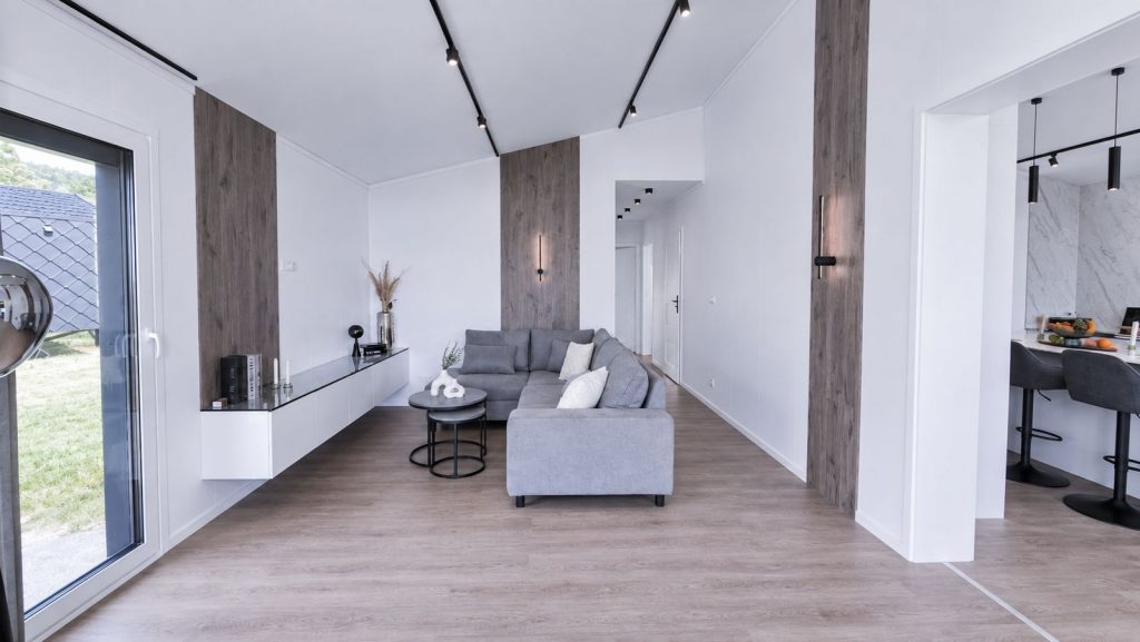 Wohnzimmer mit grauer Ecksofa-Landschaft, schwebendem Sideboard und schwarzer Schienenbeleuchtung - mobiles Eigenheim.