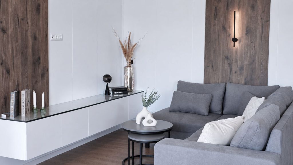 Wohnzimmer mit grauem Sofa, weißem Sideboard und Holz-Akzentwänden im gedämmten Ganzjahreshaus.