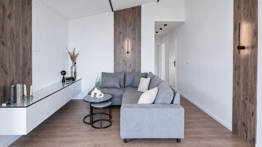 Wohnzimmer mit grauer Ecksofa-Landschaft, Holzpaneelen und Design-Wandleuchten als mobiles Eigenheim.