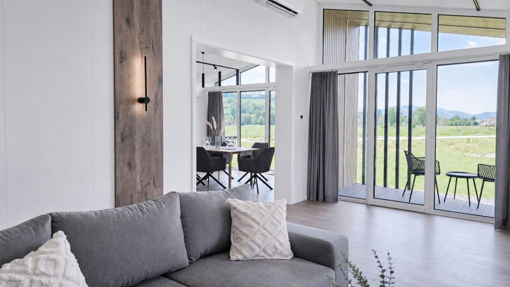 Wohnzimmer mit Ecksofa, Holzpaneel und Balkon mit Blick ins Gruene, grosszuegiges Modulhaus, verfuegbar in Bregenz.
