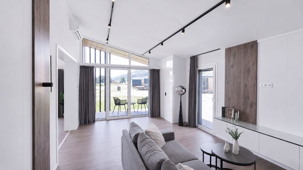 Lichtdurchfluteter Wohnraum mit grauem Sofa und Terrassenzugang im Ganzjahreshaus, verfuegbar in Oberoesterreich.