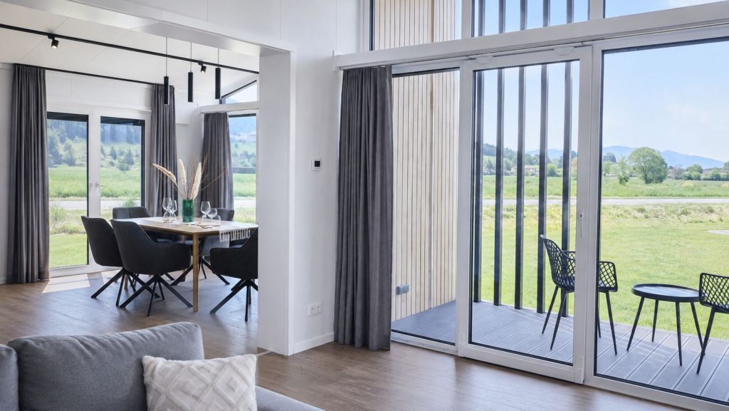 Essbereich mit Holztisch, dunklen Stuehlen und raumhoher Verglasung zur Terrasse - Ganzjahreshaus, Lieferung nach Wiener Neustadt.