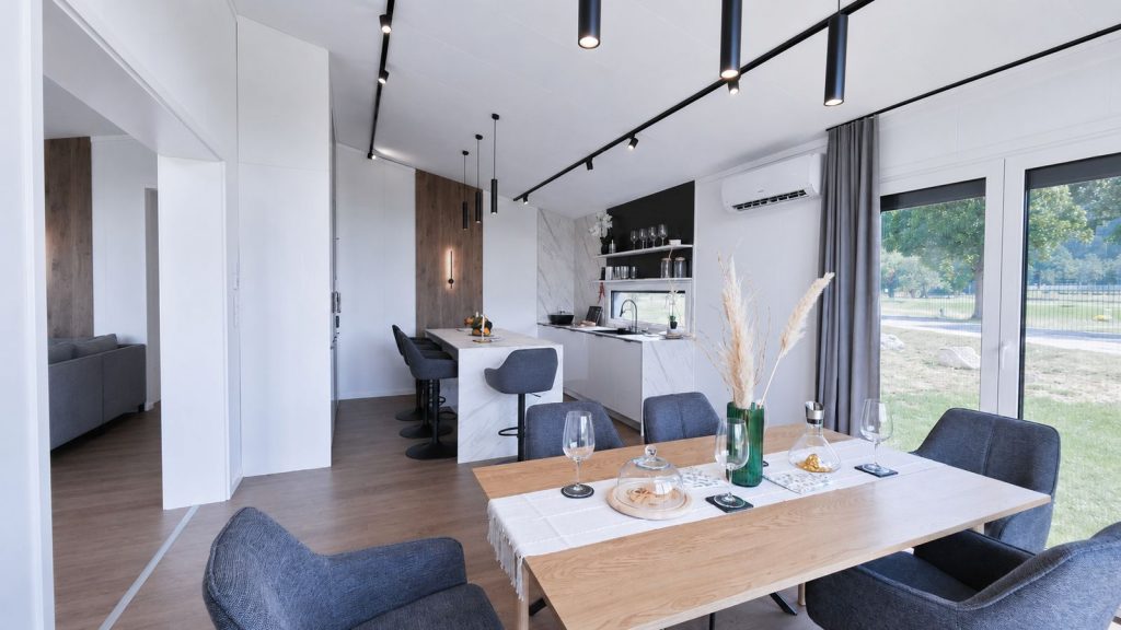 Essbereich im Diamond Vario Deluxe mit gedecktem Holztisch, Kuecheninsel und Fensterfront zum Garten - schluesselfertig fuer Tirol.