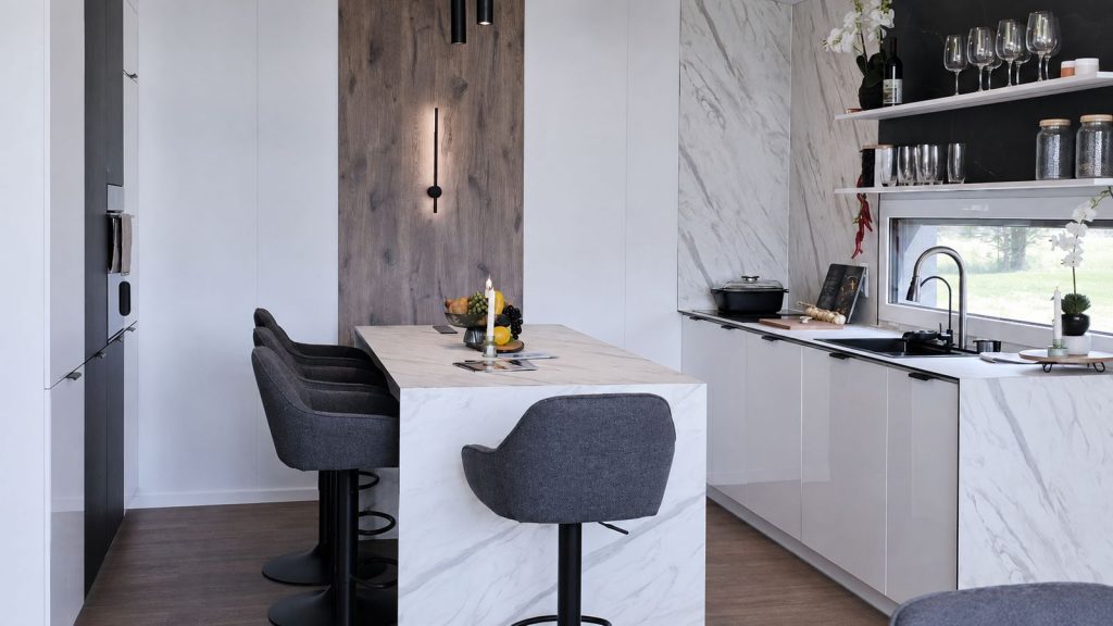 Premium-Küche im Diamond Vario Deluxe mit Marmorinsel, Barhockern und Holzakzent als Ausdruck der Massivmodul-Architektur.