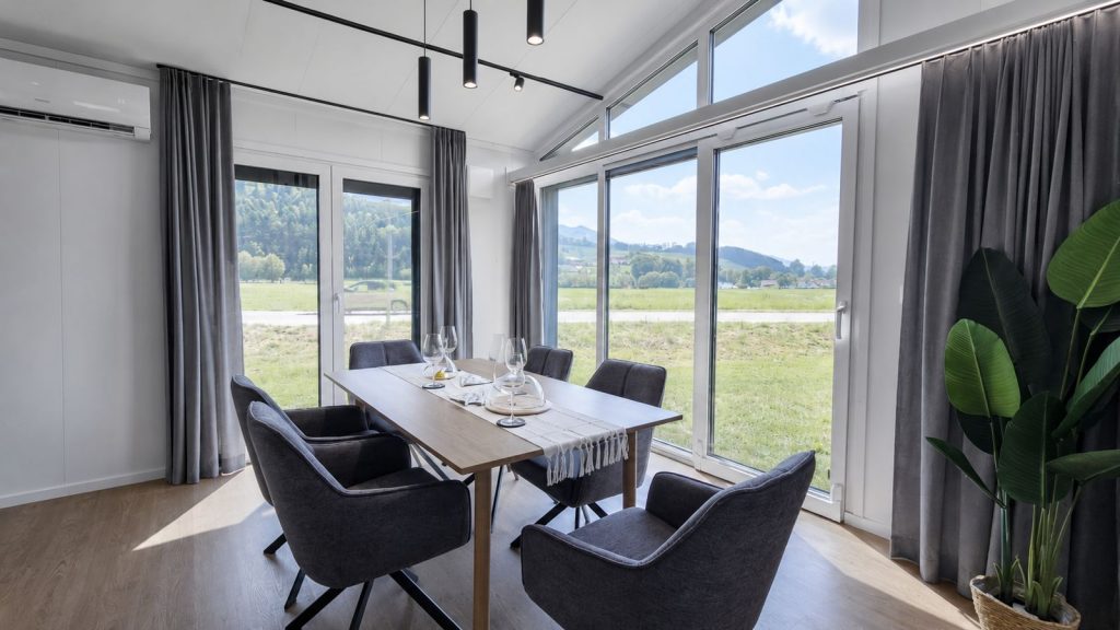 Essbereich mit Holztisch fuer sechs, Panoramaverglasung und Pendelleuchten - Premium-Mobilheim mit Lieferung nach Bregenz.