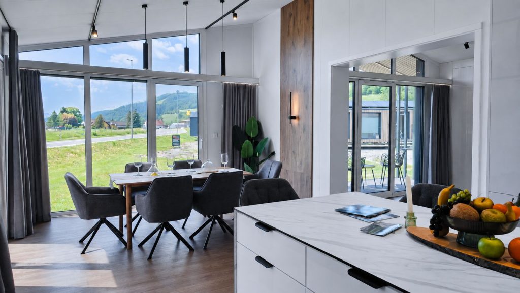 Essbereich mit bodentiefen Fenstern, Polsterstühlen und Marmorinsel mit Terrassenblick - stilvolles Premium-Mobilheim.