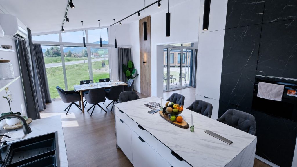Offene Küche mit Marmorinsel und Essplatz im Diamond Vario Deluxe vor Panoramafenstern, Fertighaus mit Lieferung nach Bregenz.