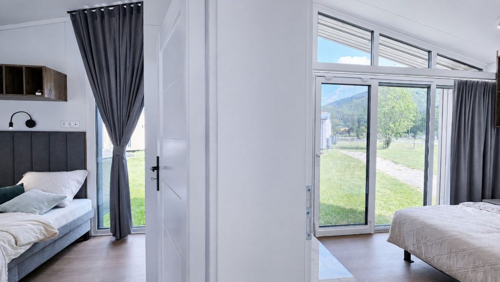 Schlafzimmer mit Polsterbett, Panoramafenstern und Blick ins Gruene - Massivmodul-Architektur, Lieferung in die Steiermark.