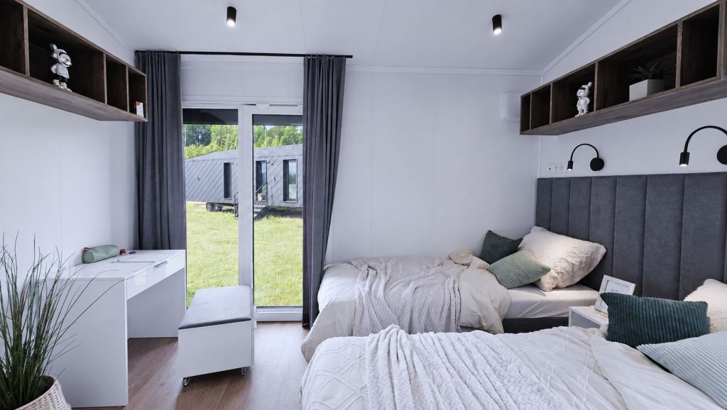 Kinderzimmer mit zwei Einzelbetten, Holzregalen und Schreibtisch, Massivmodul-Architektur - verfuegbar in Oberoesterreich.