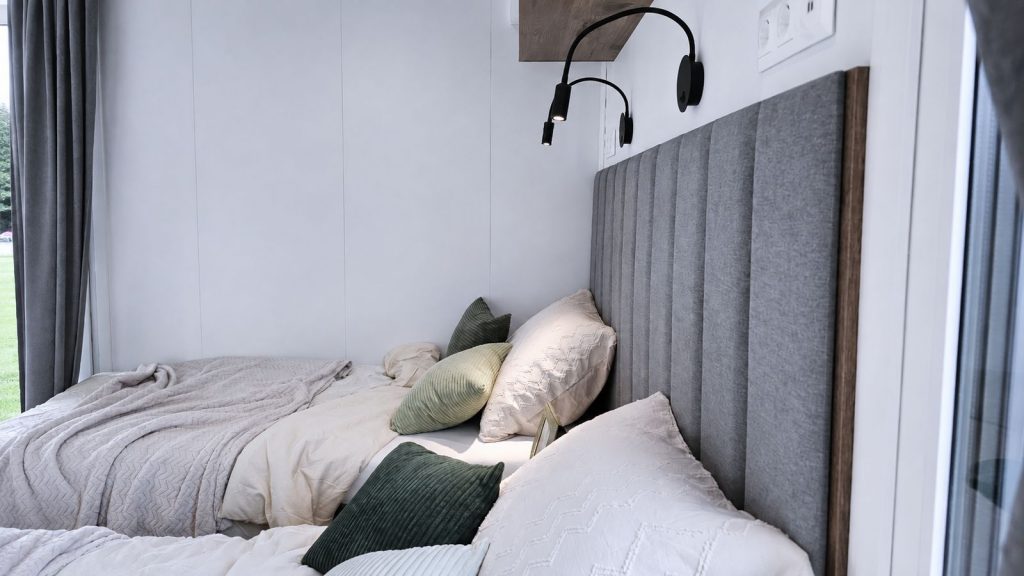 Schlafzimmer mit gepolstertem Kopfteil, Leselampen und grünen Kissen - modernes Eigenheim, verfügbar in Vorarlberg.