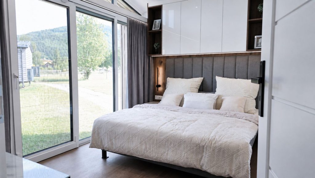 Schlafzimmer mit Doppelbett, Holzakzent und Bergblick in solider Massivmodul-Architektur, fuer Kaernten.