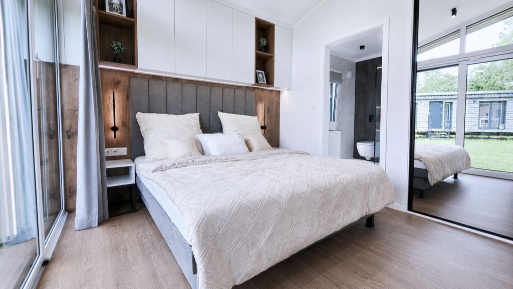 Schlafzimmer mit Doppelbett, Holzakzenten und angrenzendem Bad im Diamond Vario Deluxe, Premium-Modulhaus für Krems.